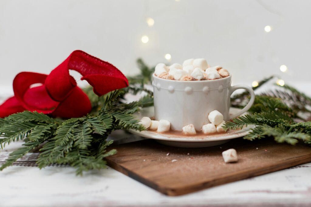 A cup of hot chocolate surrounded by pine branches and red ribbon.