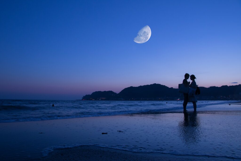 Couple silhouette on beach under half moon