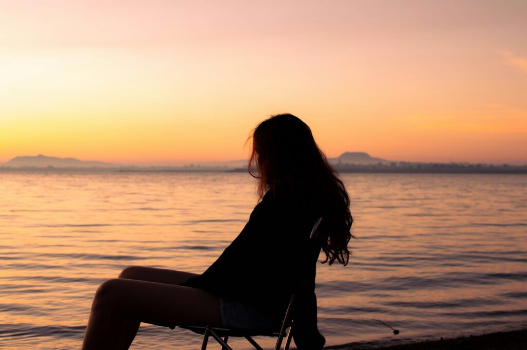 woman sitting and looking at the sunset in front of a lake