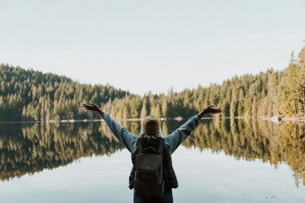 A woman standing in front of a lake with her arms open