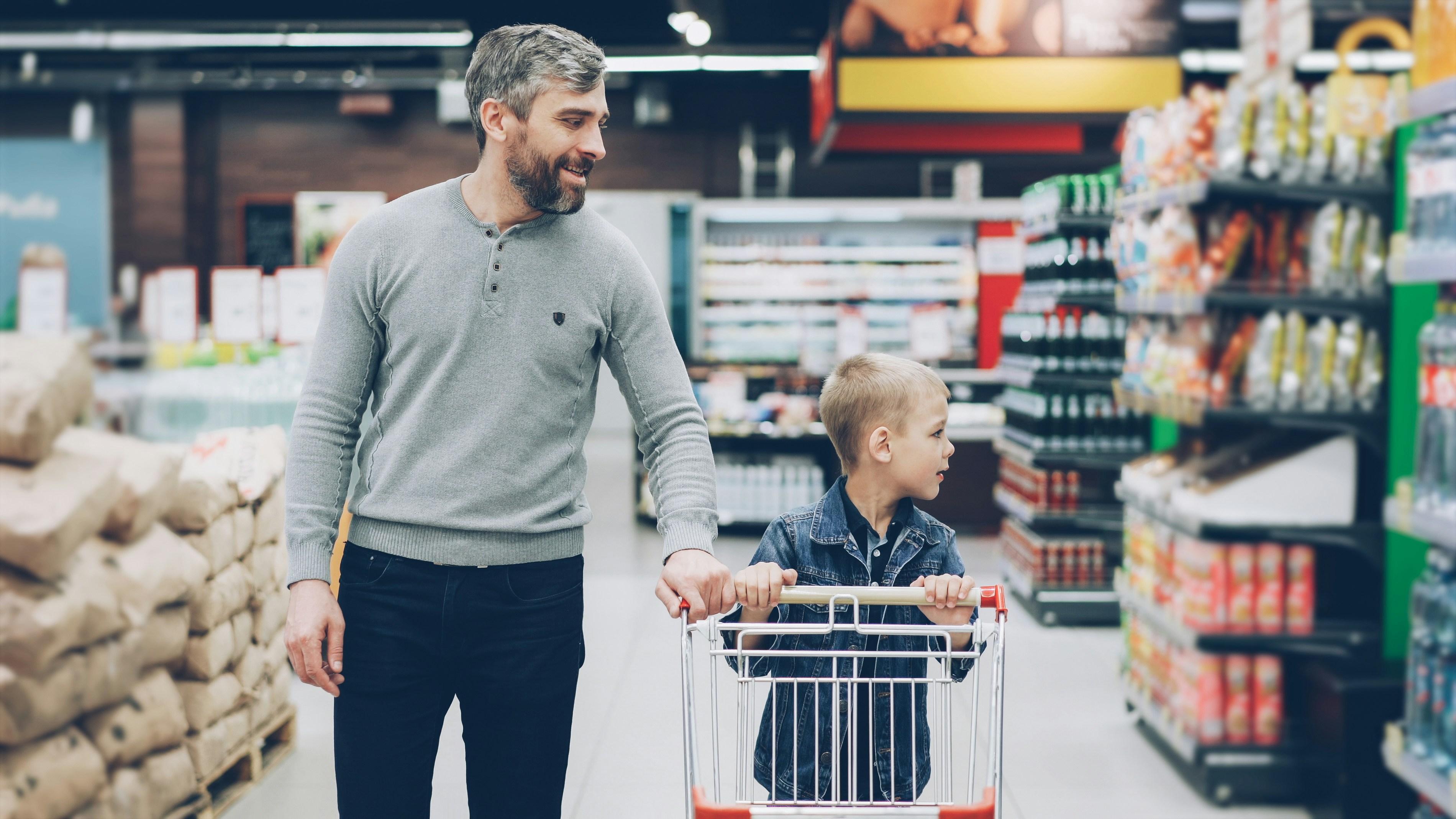 A father and son push a cart through the grocery store.
