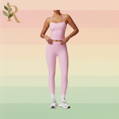 A woman wears a light pink spaghetti strap top and long matching leggings with white tennis shoes as her Pilates outfit against the Revivalist branded background.