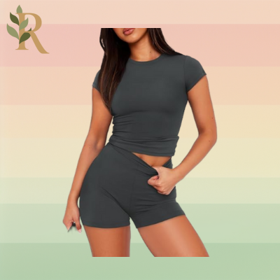 A woman wears a gray short sleeved short and short set as her Pilates outfit against the Revivalist branded background.