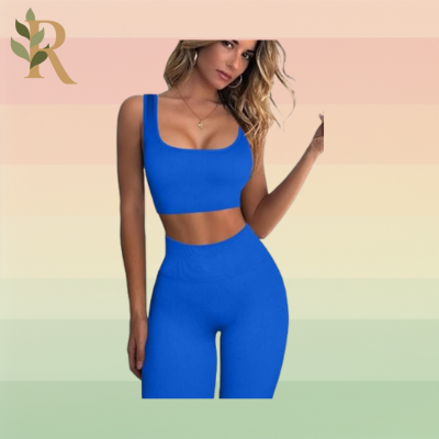 A blonde woman wearing a golden necklace wears a blue sports bra and matching leggings set as her Pilates outfit against the Revivalist branded background.