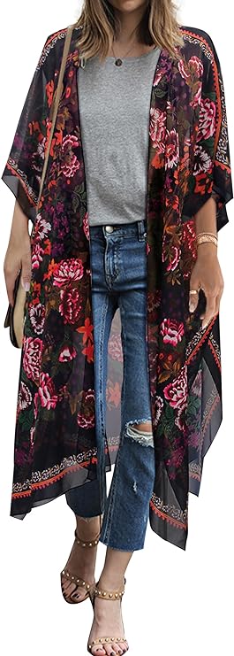 A woman stands in a gray t-shirt and jeans while wearing a black knee-length kimono with pink, red and orange flowers on it.