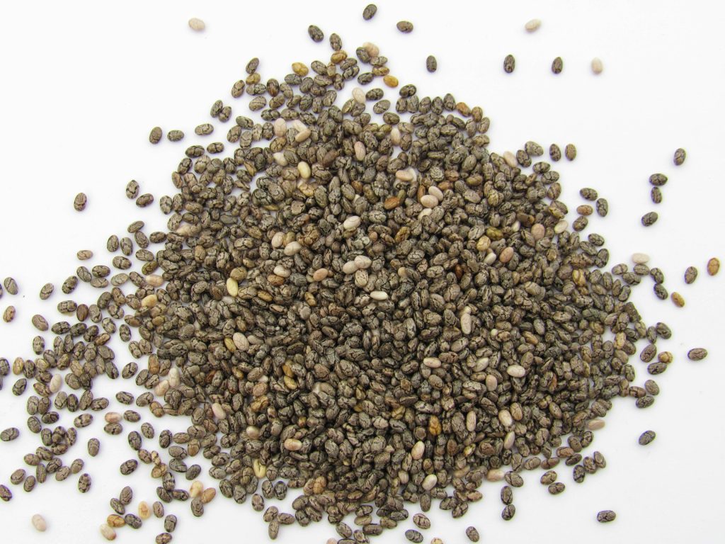 A handful of brown and white chia seeds sit on a white surface.