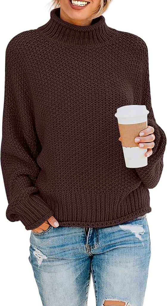 A woman stands in a brown chunky knit sweater and ripped jeans while holding a to-go coffee cup against a white background.
