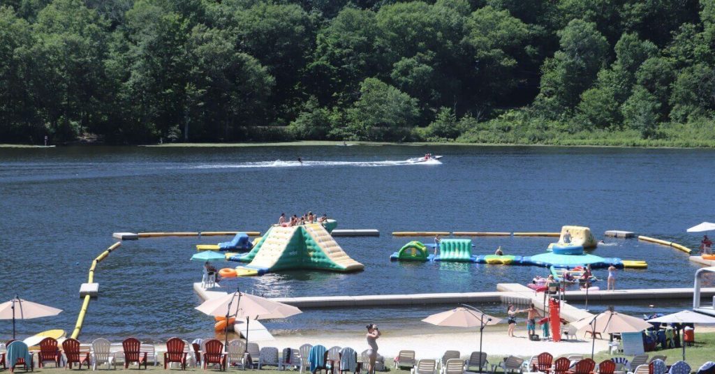 Club Getaway's lake is full of people swimming, relaxing, boating and playing on floating watersports equipment.