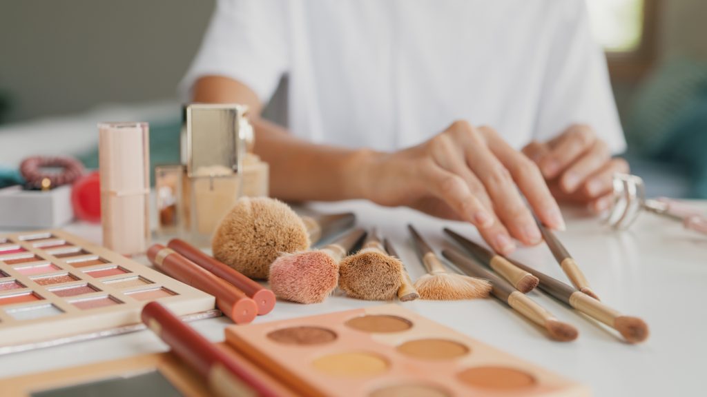 A woman sitting at a vanity strewn with makeup