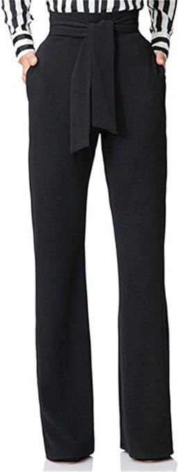 A woman stands in a black and white striped shirt tucked into black dress pants with a large tie at the waist.