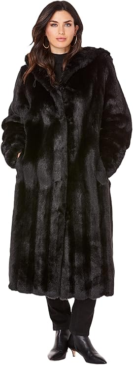 A woman wears large gold hoop earrings and a black fur coat that stretches to her knees, plus black pants and black boots with gold mini heels.