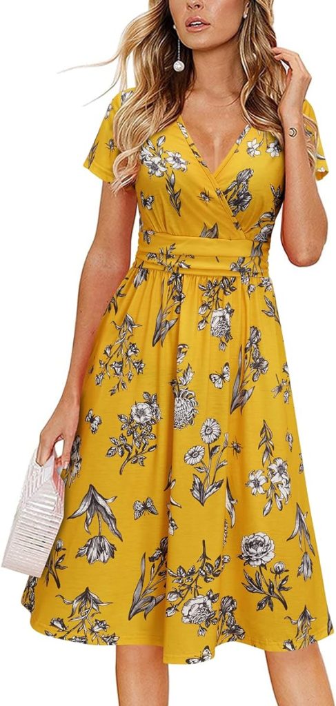 A woman stands in a yellow floral midi sundress with a v-shaped neckline and a wrap around the torso.