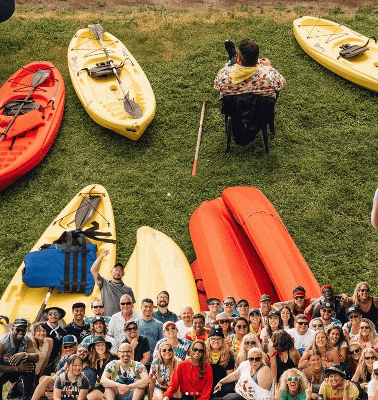 A person relaxes in a yard chair among kayaks while a group photo sits on top of the image's bottom side.