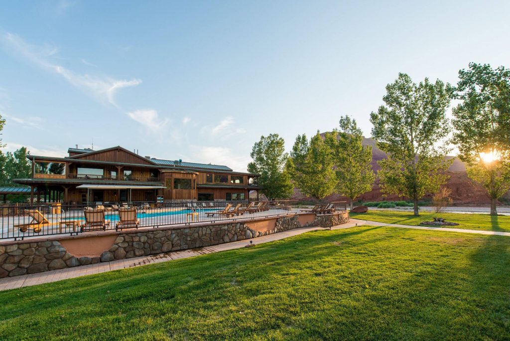 The Sorrel River Ranch pool sits under a blue sky surrounded by green grass and trees.