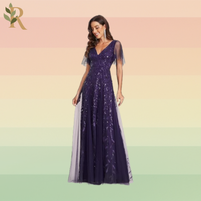 A woman stands in a purple evening gown covered in floral sequins and mesh quarter-length sleeves as one of the fall wedding guest dresses people might wear this year.