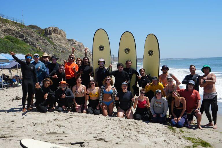 People pose with surfboards on a beach after finishing an adult summer camp with Endless Summer Surf Camp.