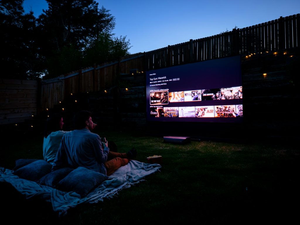 A man and woman watch a movie in a backyard.