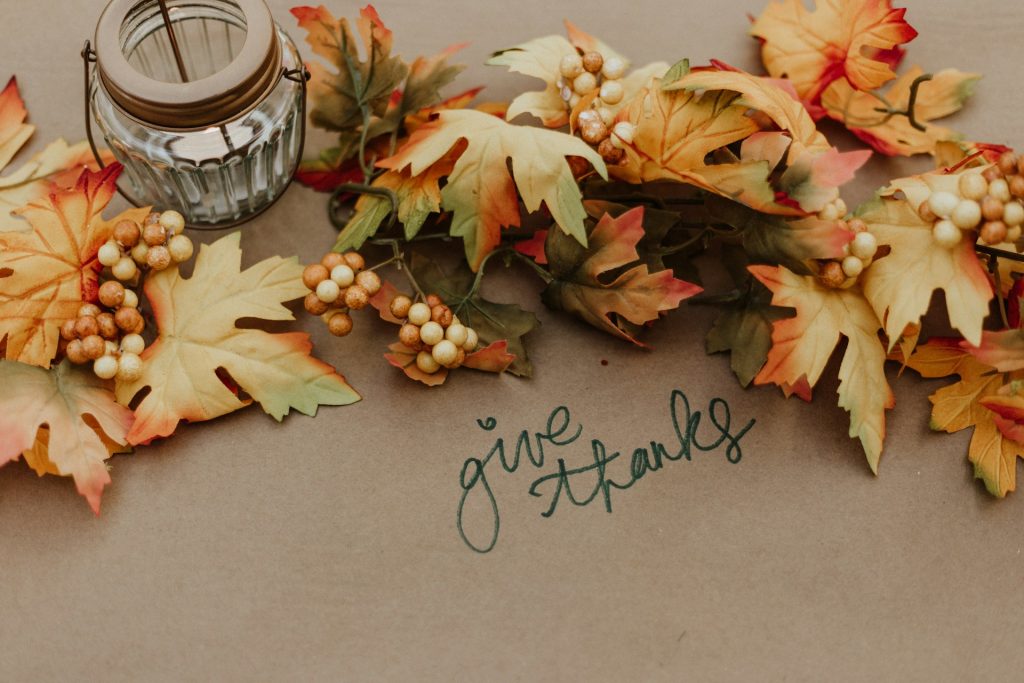 Faux greenery stretches across a table with a candle in the middle. The words "Give Thanks" in cursive sit underneath the greenery.