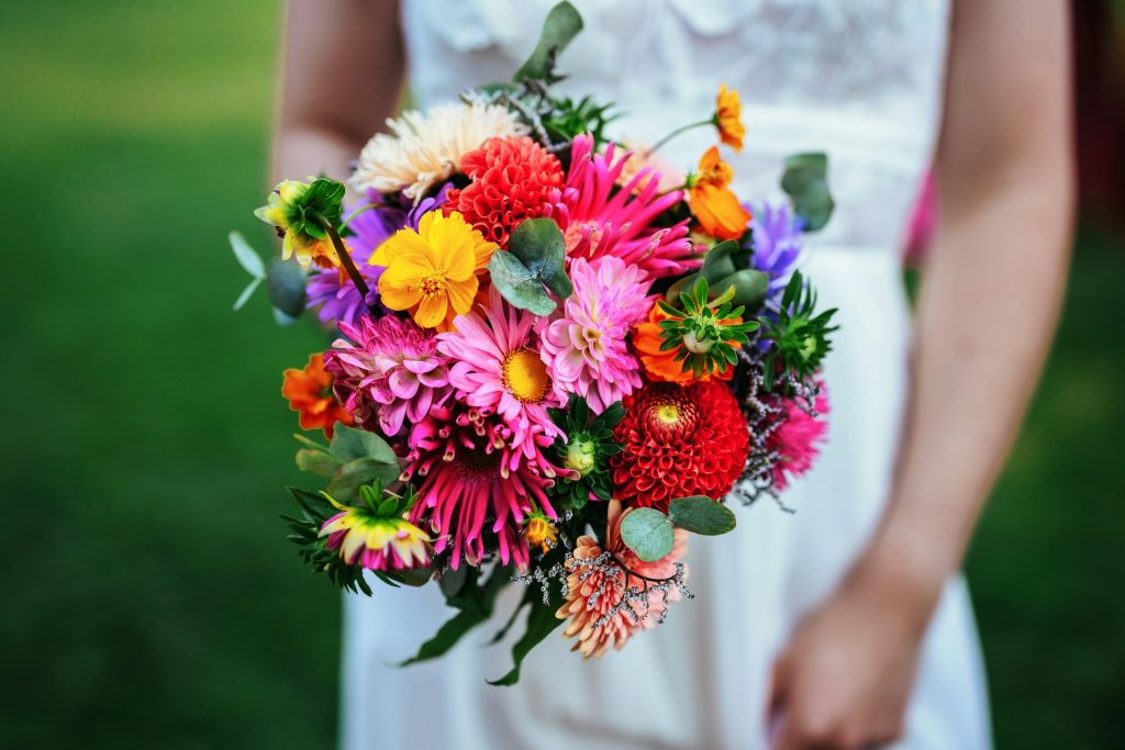 A bride holding a bouquet of bright pink, red, yellow and green florals.