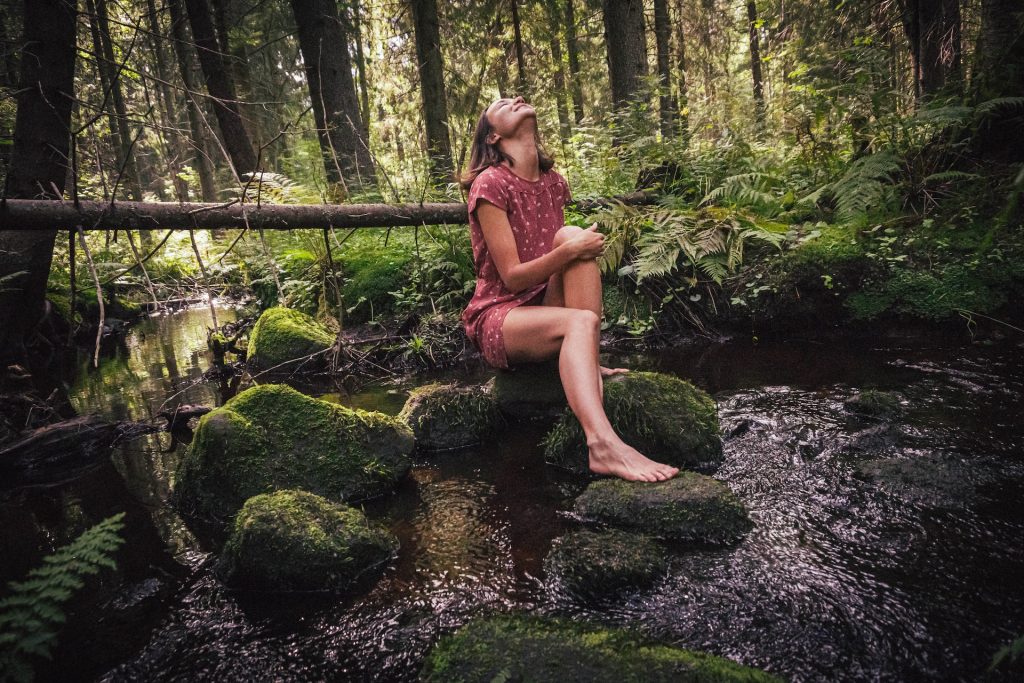 A woman sits on a rock in the forest.