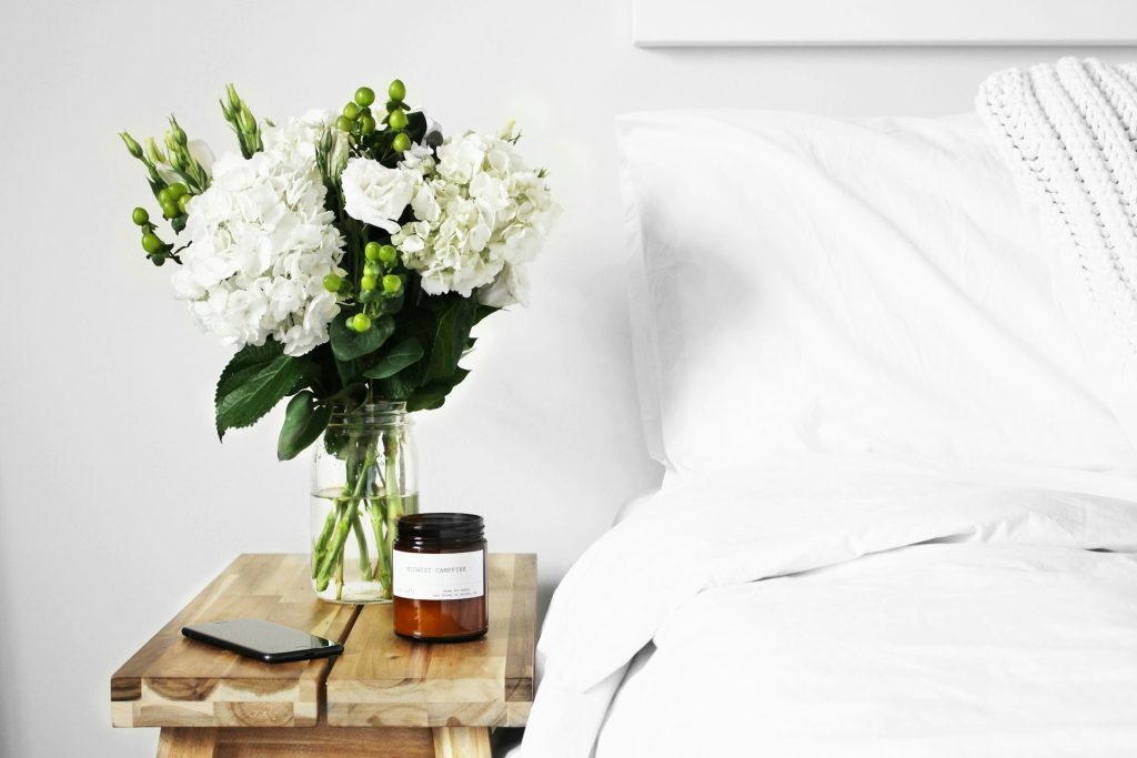 A bedside table with a phone, candle and flower vase.