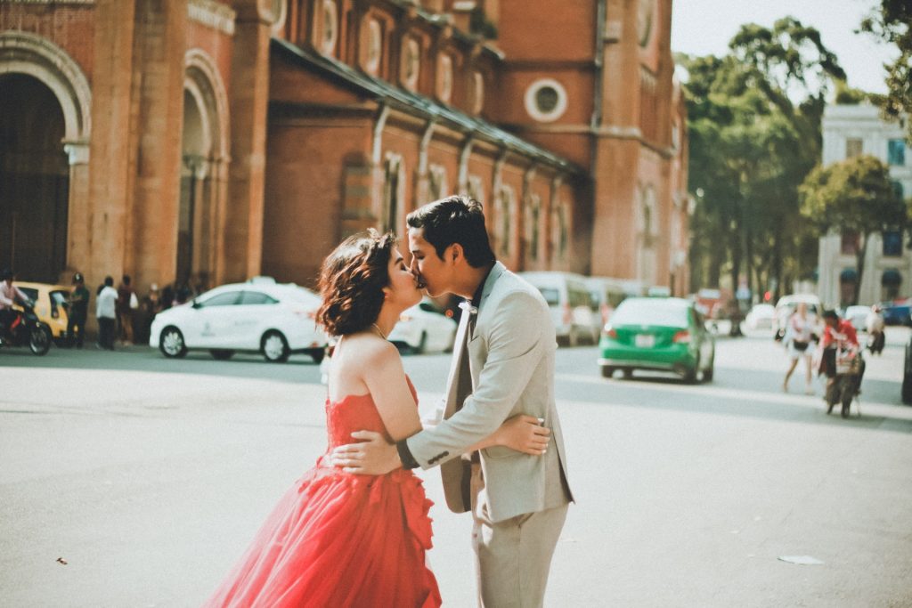 A woman wearing a red gown and a man wearing a gray suit kiss.