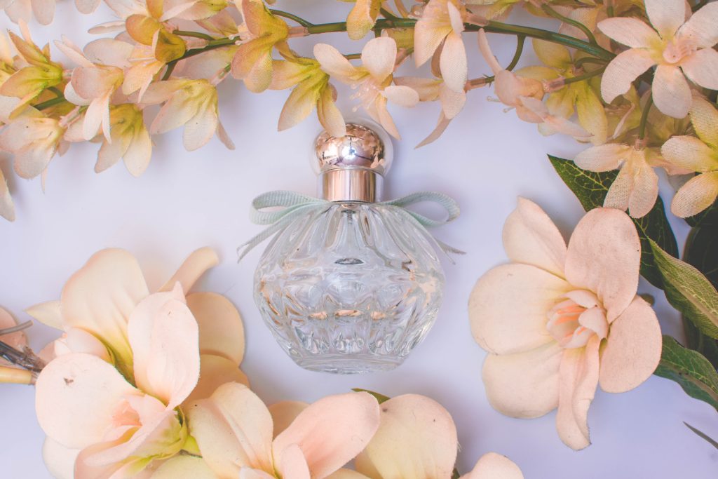 A perfume bottle sits surrounded by flowers.