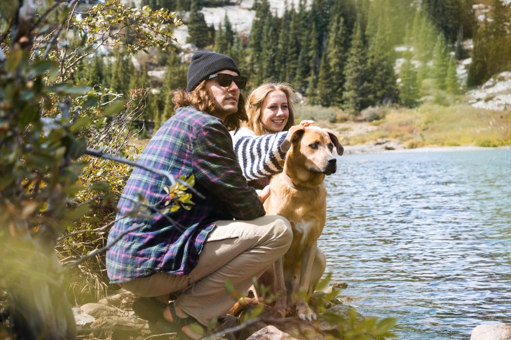 A man, woman and dog sit at the edge of a river.