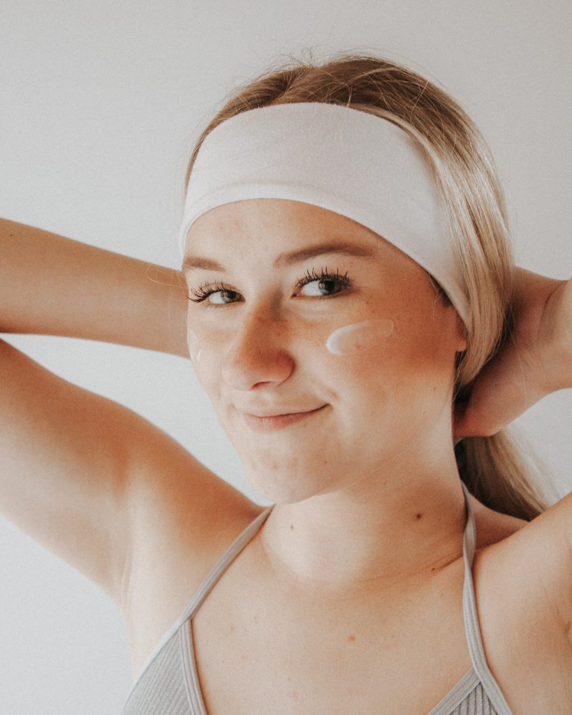 A woman with blonde hair applies moisturizer to her skin.