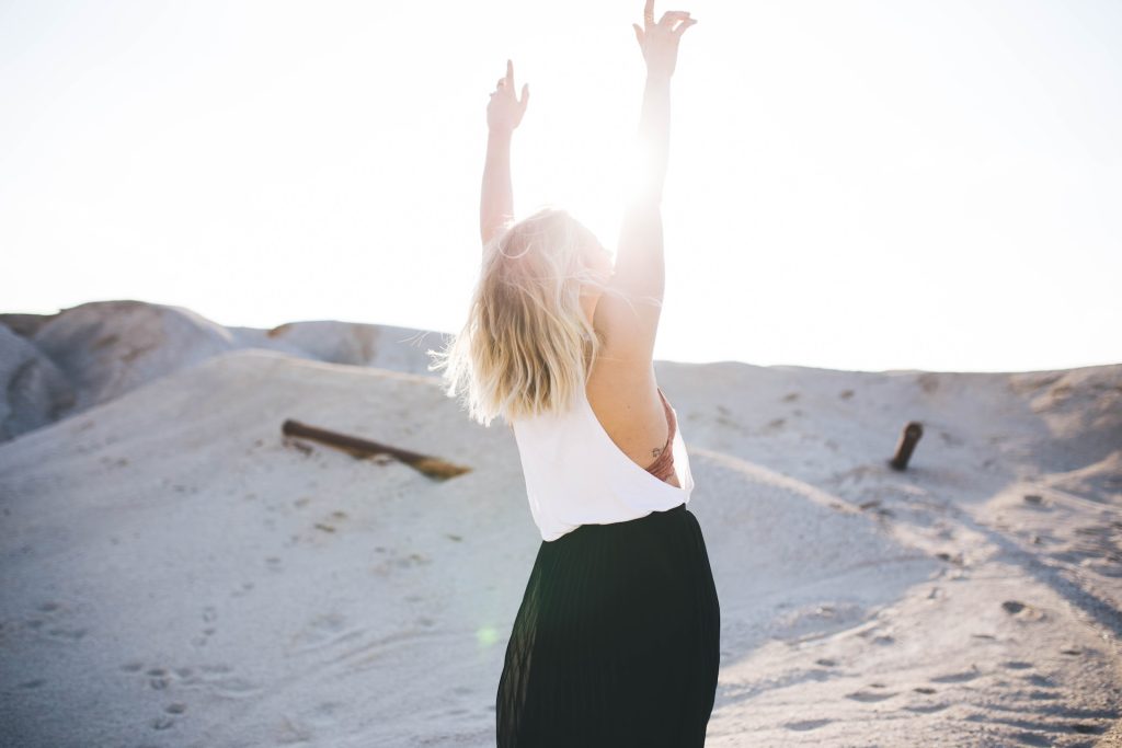 A woman stands with her arms raised in the sunlight.
