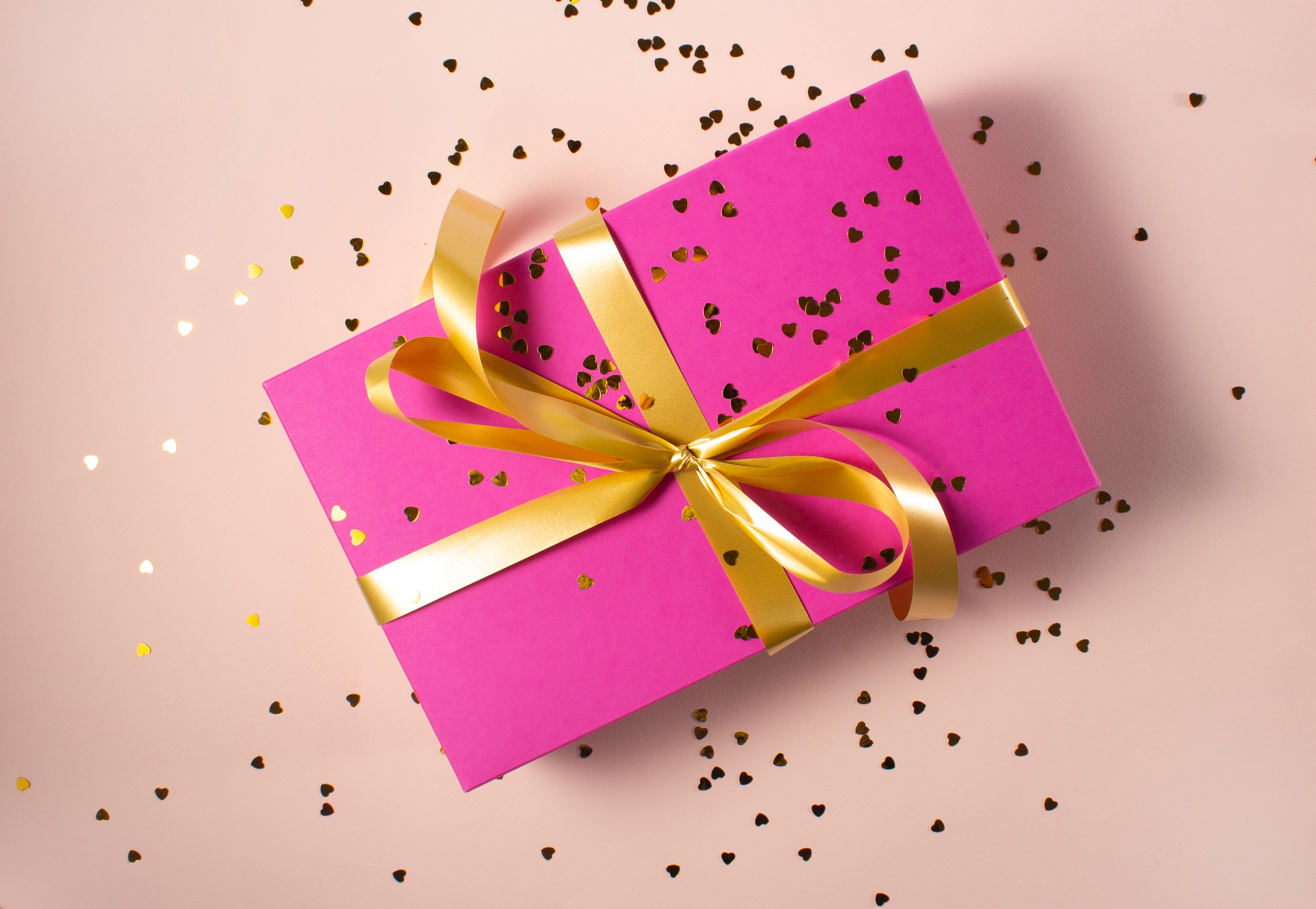 A gift is wrapped in pink paper with a golden bow and confetti.