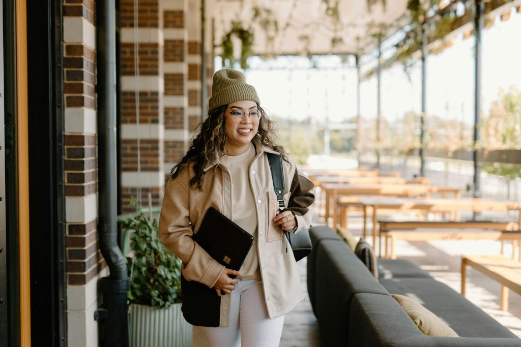 A woman smiling holding a bag and a laptop.