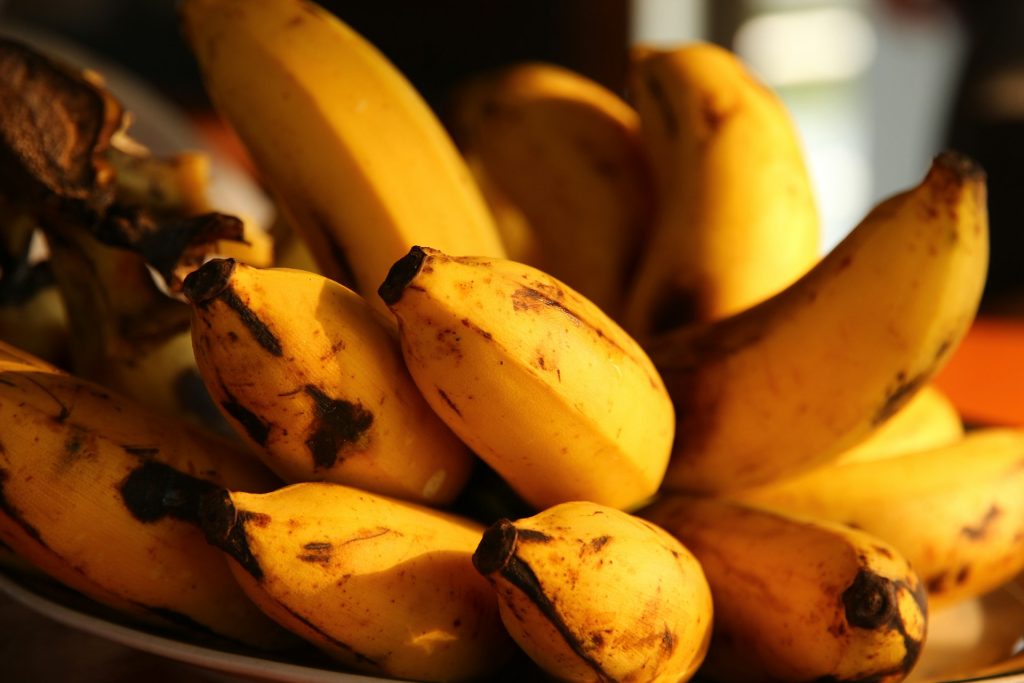 An unbroken bunch of bananas sits on its side in a bowl. The bananas are bright yellow with brown flecks around the bottom.