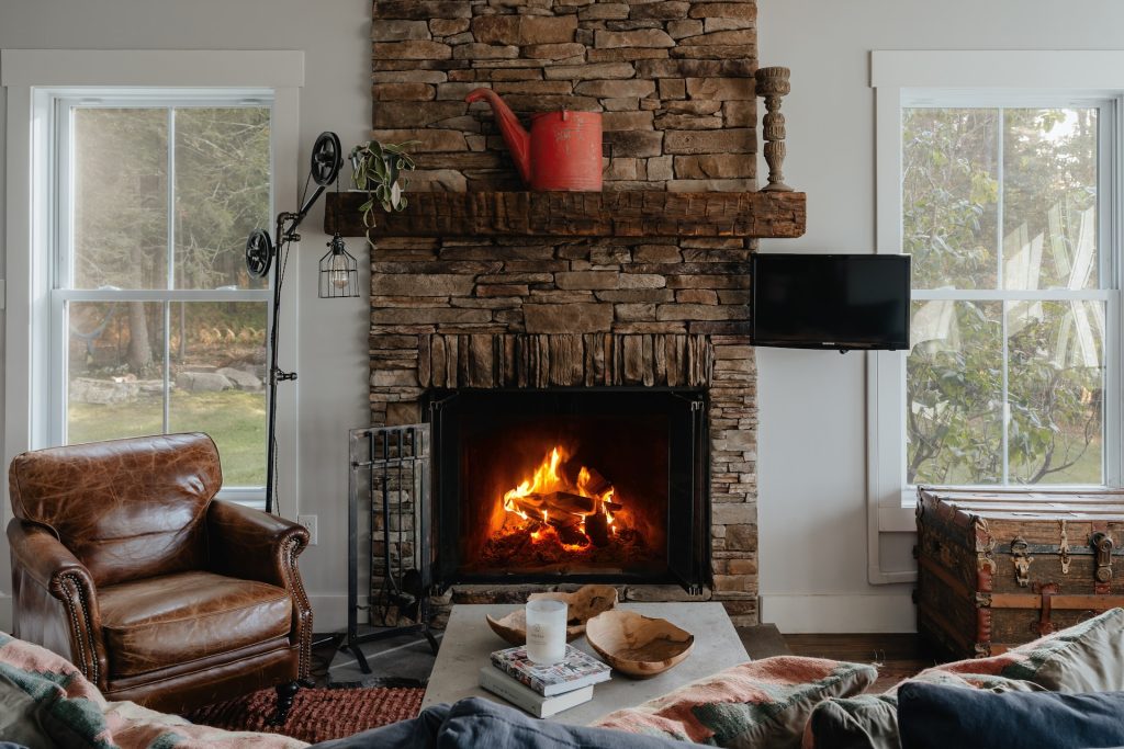 A vintage watering can and stone statue sit on a fireplace mantle.