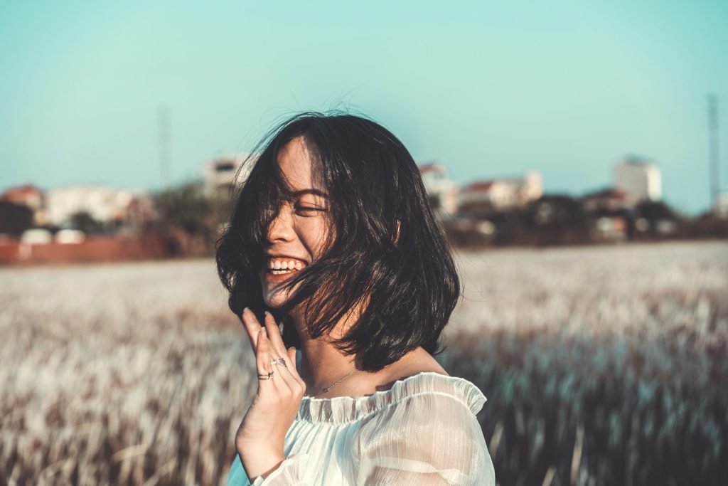 A woman with short black hair smiles and stands in a field.