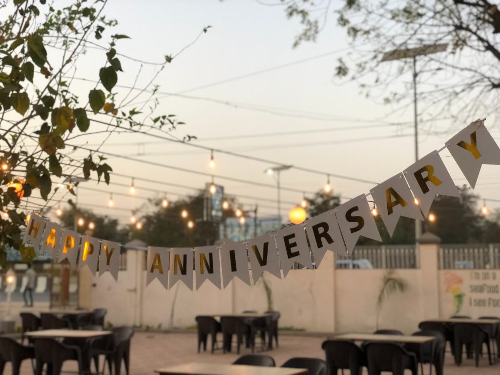 A banner reading "happy anniversary" hangs over tables outside.