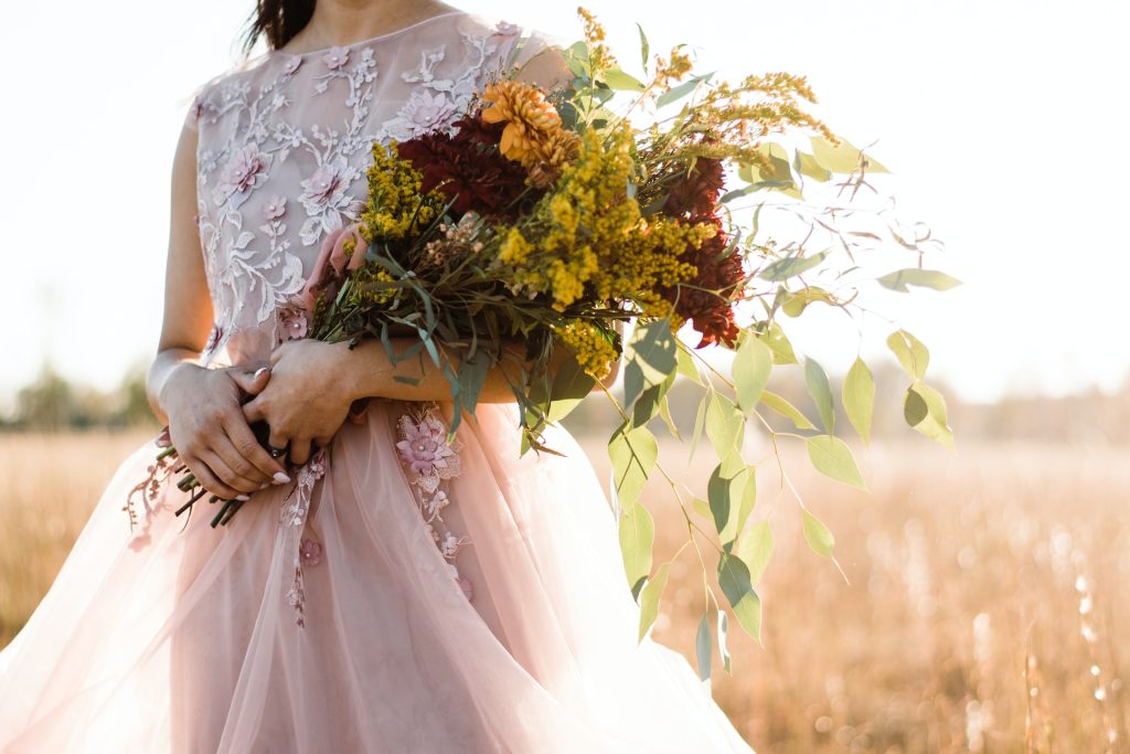 A woman wearing a pink, floral gown holds a bouquet.
