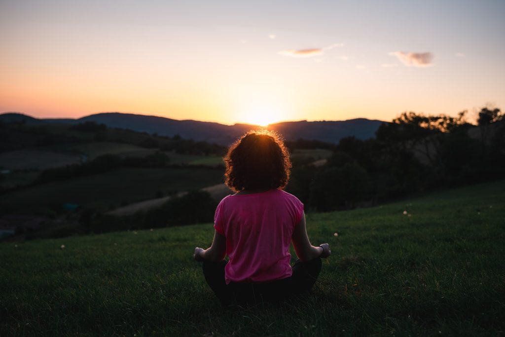 A woman meditates outside overlooking the sunset.