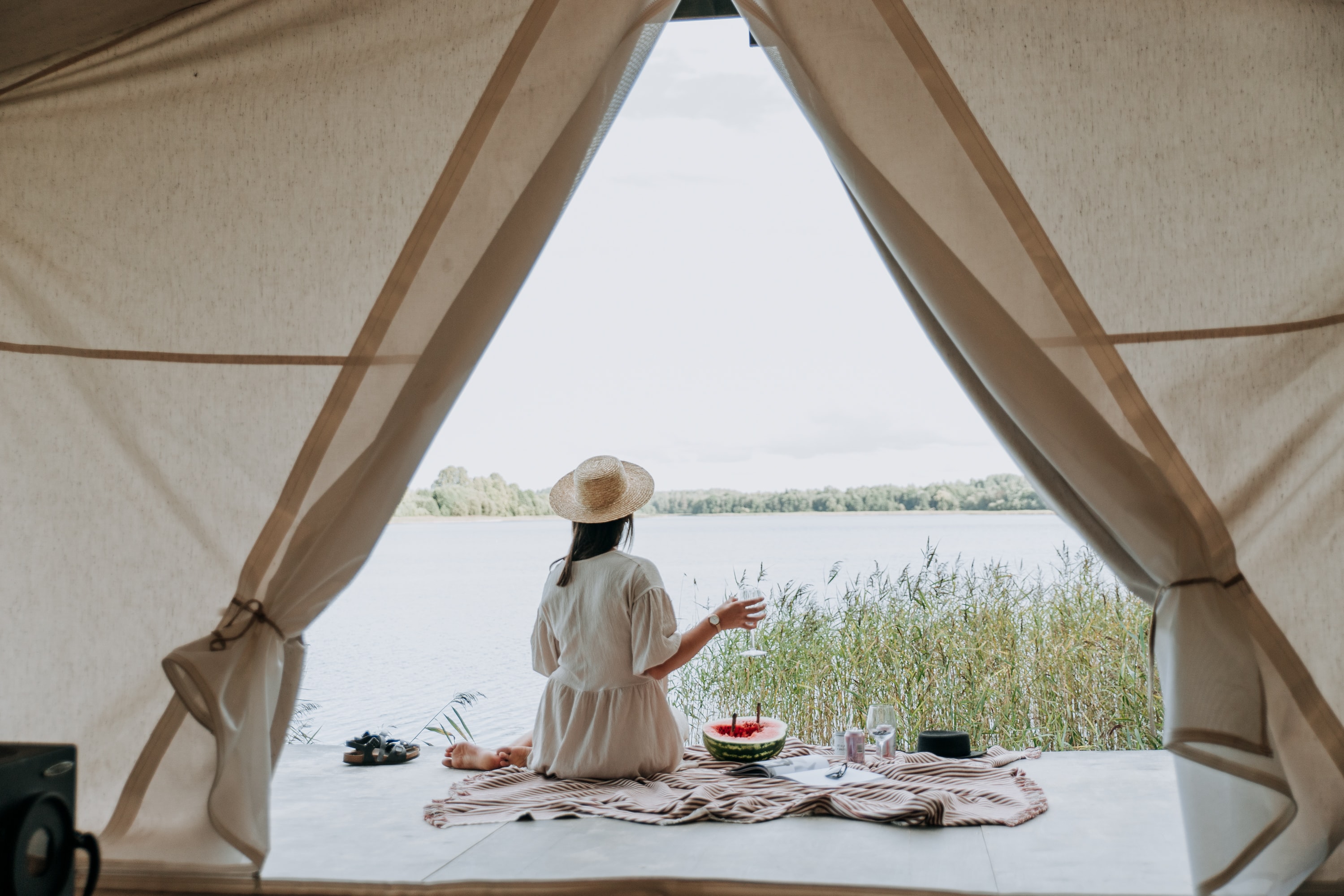 A woman sits outside of a tent with a glass of wine.
