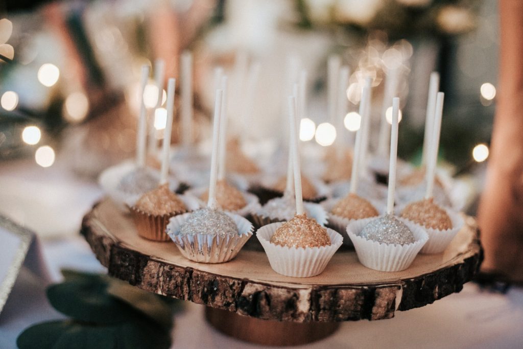 Gold and silver cake pops sit on a wooden tray as the centerpiece of a table.