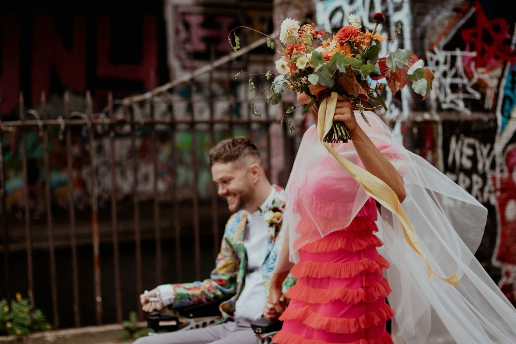 A bride wearing a pink dress and a groom in a wheelchair wearing a floral suit.