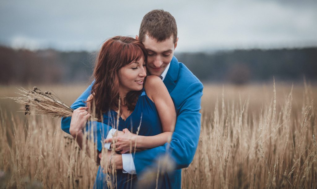 A man in a blue suit and a woman in a blue dress embrace.