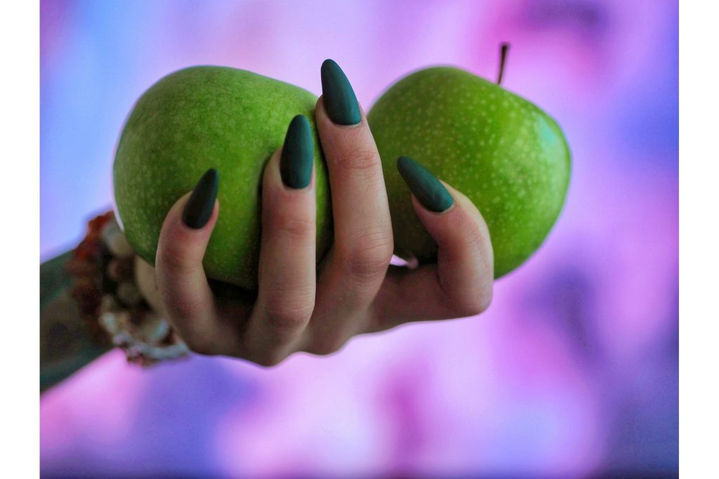 A hand with green nails holding apples
