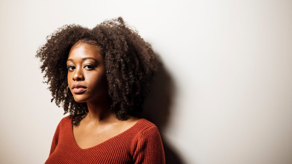 A woman with black curly hair looks at the camera.