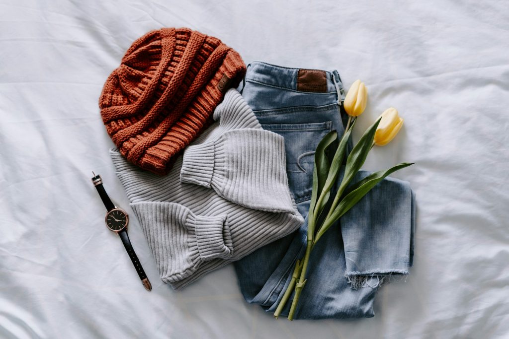 A sweater, jeans and hat laid out on a bed.