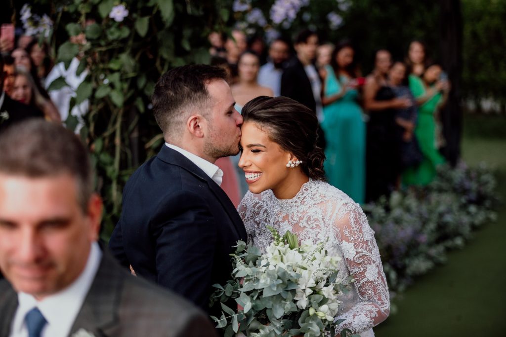 A groom kisses a bride on the forehead.