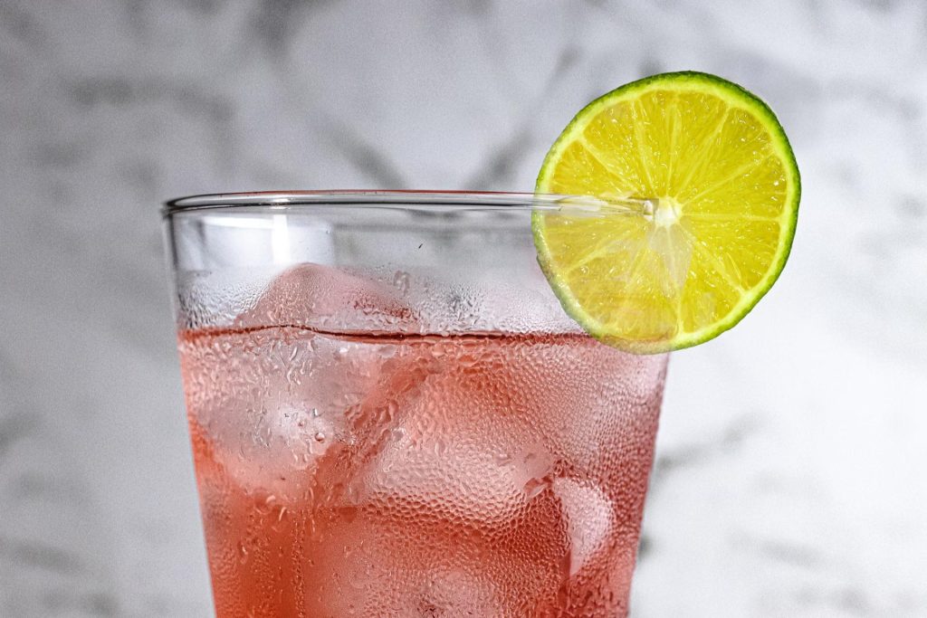 orange-red drink in glass with lime slice