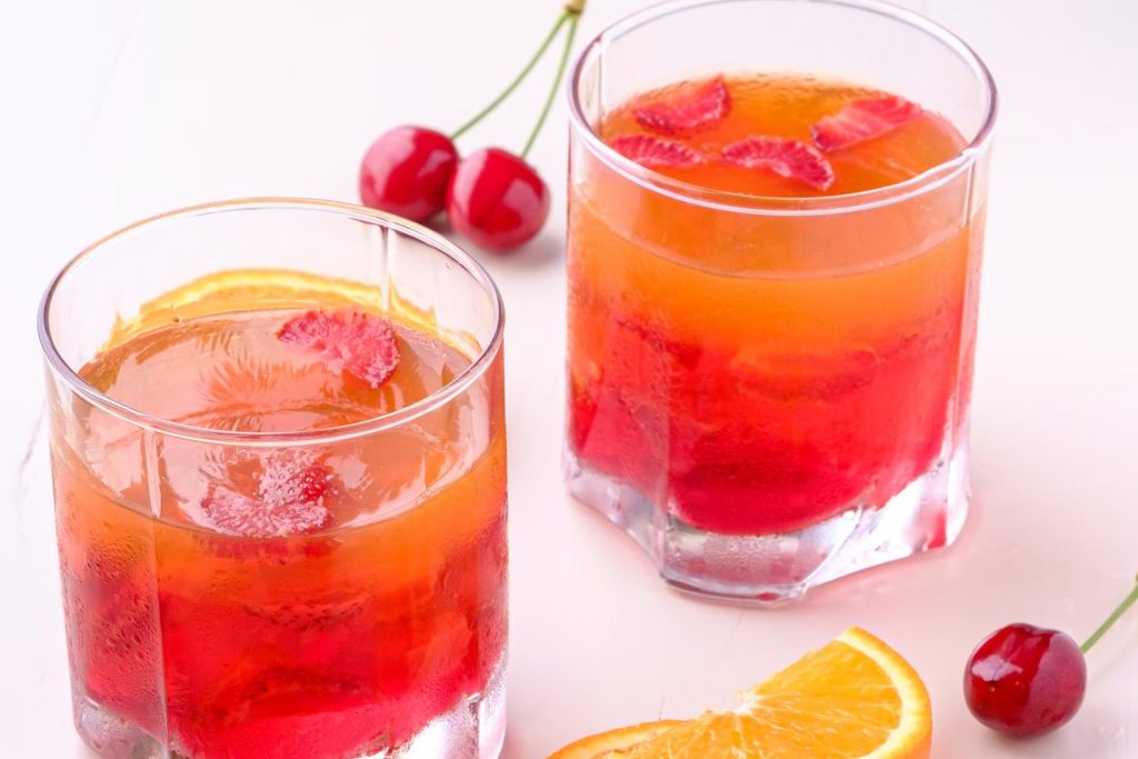 red and orange drinks with cherries and orange on the table
