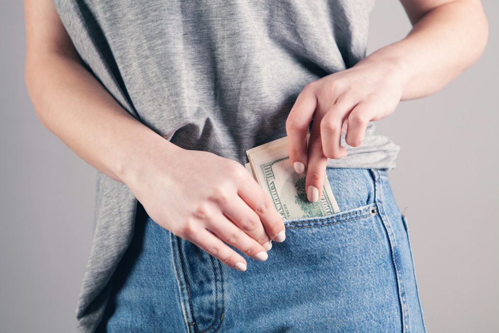 woman putting $100 bills in her jean pocket