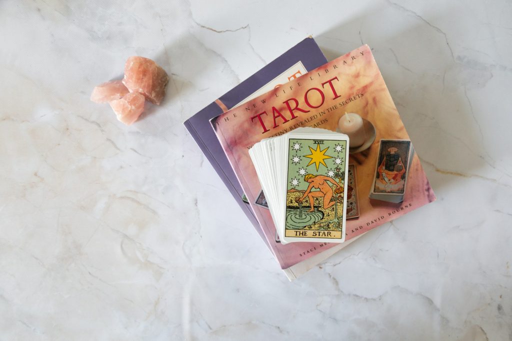 Tarot card books and a deck of cards sit on a white marble counter next to pink crystals. They likely explain the meaning behind each life path number.